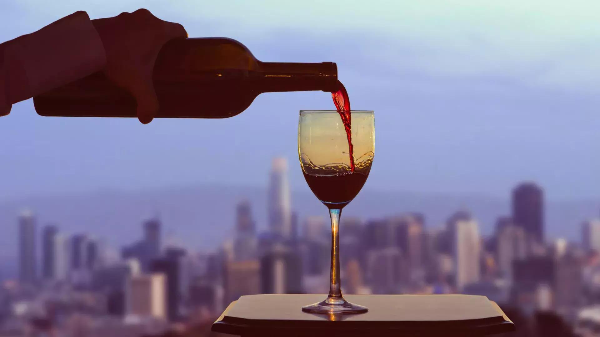 窓の外にはサンフランシスコのスカイラインが見える中、グラスに赤ワインが注がれています。