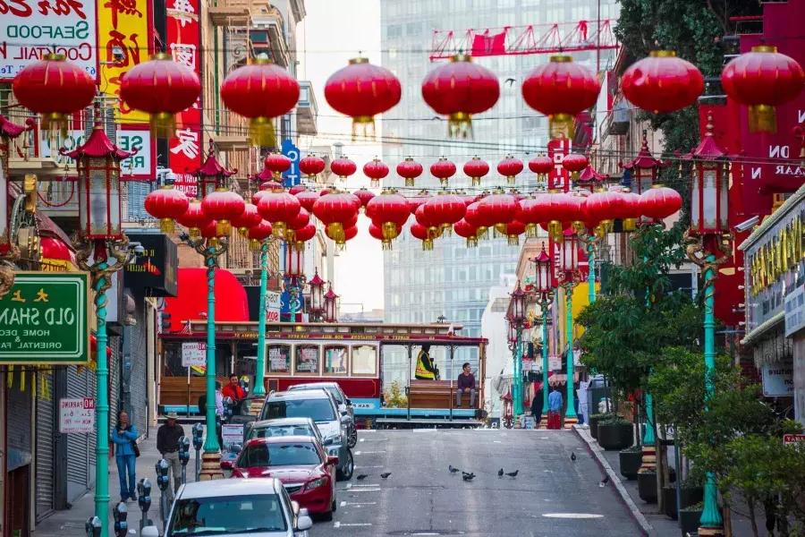 Une rue vallonnée du quartier chinois 贝博体彩app est représentée avec des lanternes rouges suspendues et un tramway qui passe.