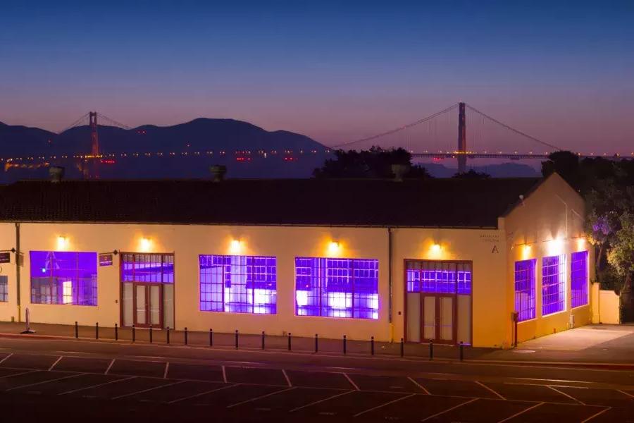 梅森堡的建筑在晚上被紫色的室内照明照亮。, im Hintergrund ist die Brücke zu sehen.