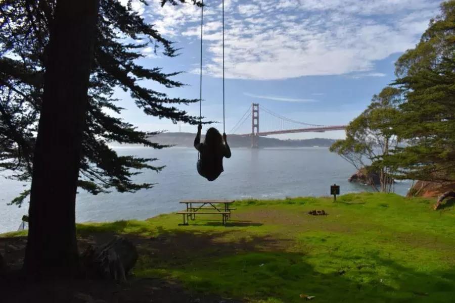 Uma mulher balança em um balanço de árvore 和 vista para a Ponte Golden Gate. 加州贝博体彩app.