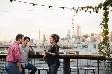 Three people gather around an outdoor table on the roof deck of Anchor Distilling 在贝博体彩app, 加州.