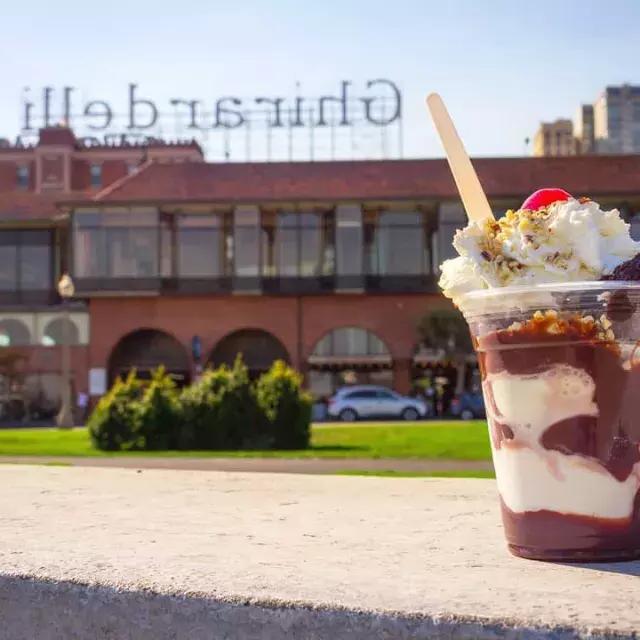 A chocolate sundae sits in the foreground with Ghirardelli Square in the background.