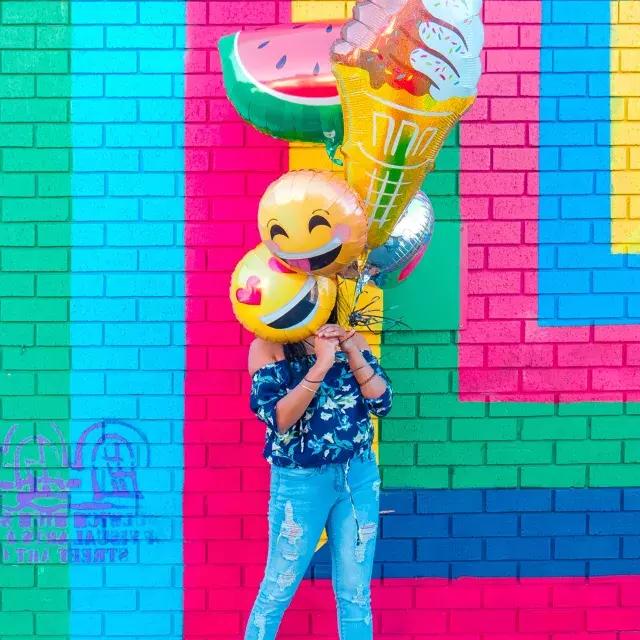 女の子がカラフルな壁画の前で風船で誕生日を祝っています。